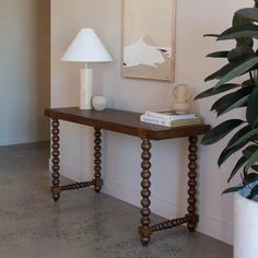 a wooden table sitting next to a plant and a lamp on top of a hard wood floor