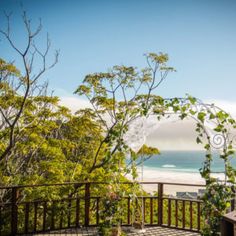 a wooden deck overlooking the beach and ocean with an arch in the middle that has vines growing on it