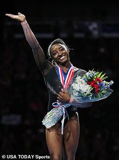 a woman standing on top of a balance beam with flowers in her hand and an award around her neck