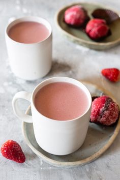 two cups of hot chocolate with raspberries next to them on a saucer