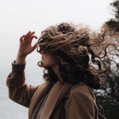 a woman with her hair blowing in the wind by the water's edge,