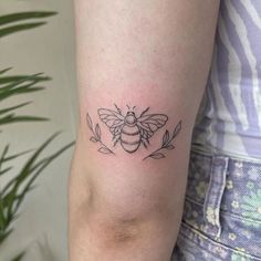 a small black and white bee tattoo on the right arm, with leaves around it