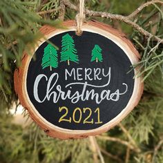 a merry christmas ornament hanging on a tree branch with pine trees in the background