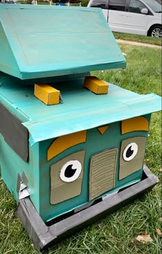 an outdoor play house made out of cardboard with eyes and nose on the top, sitting in grass