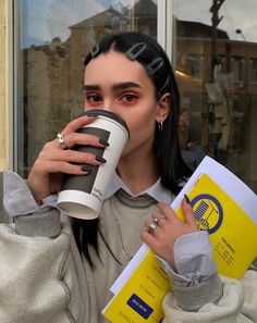 a woman drinking from a coffee cup while holding a book