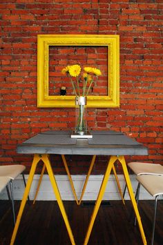 a table with yellow flowers in a vase on top of it next to two chairs