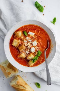 a bowl of tomato soup with bread and basil