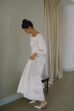 a woman in a white dress is standing on a bench and looking down at her shoes