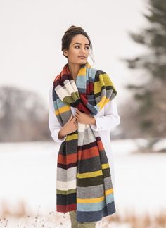 a woman standing in the snow wearing a multicolored scarf