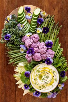 a plate with flowers, cucumbers and other vegetables on it next to a bowl of dip