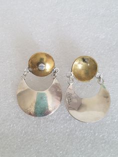 Featuring these pair of Modernist Taxco mixed metal earrings made using Brass and Silver. The round brass component has a post on the back and a screw design on the frontside and on each side it has 2 silver rings that dangle a wide Crescent moon. The Crescent moon is slightly dome and, on the backside, there is a hallmark that reads "925 T-5 Mexico". They are from the 1950's and are slightly heavy for my earlobes. They will arrive with 925 backs and are in excellent vintage condition. Drop measures: 1 3/4" X 1 1/4"W Material:  Brass, Sterling Silver Hallmark:  925 T-5 Mexico Gift box FREE SHIPPING Silver Crescent Hammered Earrings, Silver Dangle Clip-on Earrings In Brass, Nickel Free Brass Round Clip-on Earrings, Nickel-free Round Brass Clip-on Earrings, Nickel-free Silver Brass Clip-on Earrings, Crescent Moon Earrings Studs, Moon Earrings Studs, Mexico Gift, Mixed Metal Earrings