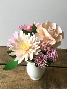 a white vase filled with flowers on top of a wooden table