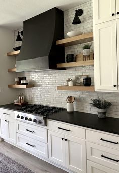 a kitchen with white cabinets, black counter tops and open shelving above the stove