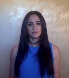 a woman with long black hair standing in front of a wall and looking at the camera