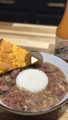 a bowl filled with beans and meat next to a bottle of beer