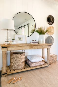 a wooden table topped with a mirror next to a lamp and wicker basket filled with pillows