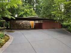 a house in the woods surrounded by trees and shrubs with a driveway leading to it