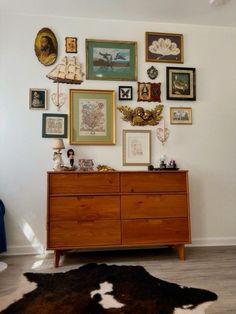 a dresser with many pictures on the wall above it and a cowhide rug in front of it