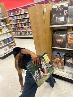 a woman is leaning over to pick up a cd from the shelf in a store