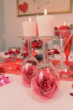 two wine glasses with roses in them sitting on a table next to candles and confetti