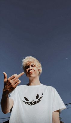 a man with blonde hair making the peace sign while wearing a white t - shirt