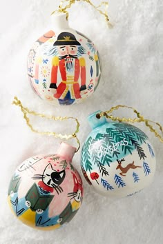 three hand painted christmas ornaments hanging on a gold chain, one with an ornament in the shape of a nutcracker