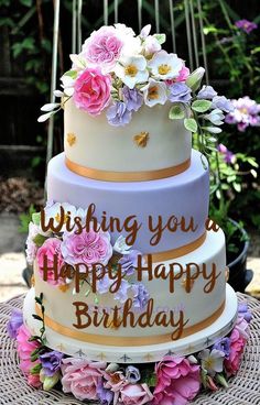 a three tiered cake with flowers on the top and writing wishing you a happy birthday