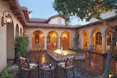 an outdoor dining area with chairs, table and fountain in front of a house at dusk