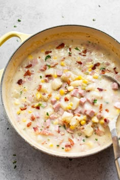 a pot filled with corn and ham chowder next to a spoon on a table