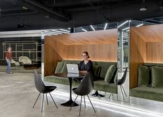 a woman sitting at a table with a laptop in front of her, while another person walks by