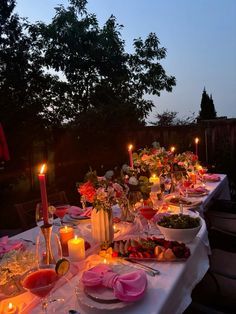 a long table is set with candles and plates full of food for an outdoor dinner