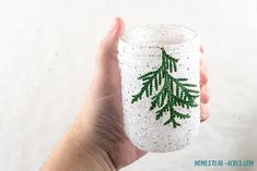 a hand holding a glass filled with white and green glittered pinecone decorations