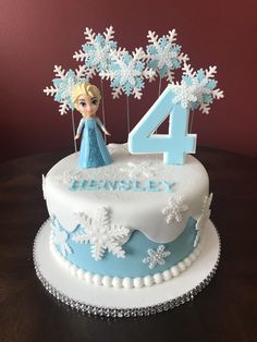 a birthday cake with a frozen princess figure on top and snowflakes around it