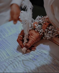 a close up of a person's hands holding a feather and flowers on top of a piece of paper