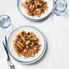 two white plates with food on them next to silver utensils and water glasses