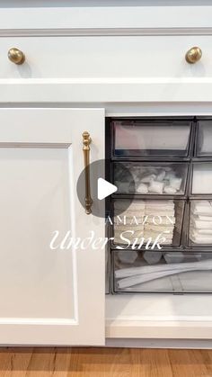 an open cabinet with clear drawers on the bottom and white cabinets below it that has gold handles