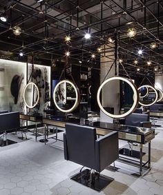 a salon with chairs and mirrors on the wall, lights hanging from the ceiling above them