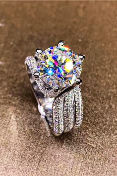 a diamond ring on top of a table with other rings around it and the center stone is surrounded by smaller diamonds