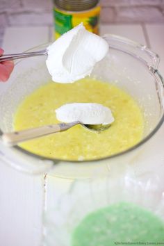 someone is spooning marshmallows into a bowl of yellow liquid with a can in the background