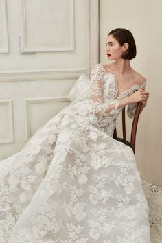 a woman sitting on top of a wooden chair wearing a white wedding dress with long sleeves