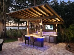 an outdoor kitchen with bar seating and lights on the grill area is lit up at night