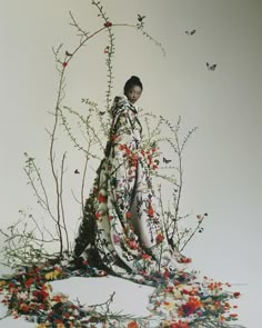 a woman standing in front of a tree surrounded by flowers and branches with butterflies flying around her