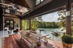 a wooden deck with a table and chairs on it next to a large window overlooking the water