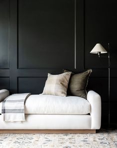 a white couch sitting in front of a black wall with two lamps on top of it