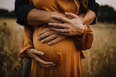 a pregnant woman holding her husband's belly in a field with tall brown grass