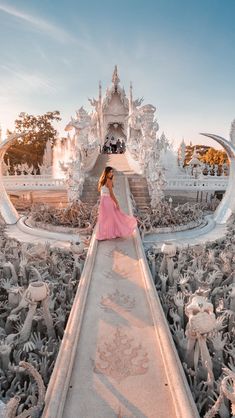 a woman in a pink dress is standing on a walkway surrounded by statues and sculptures