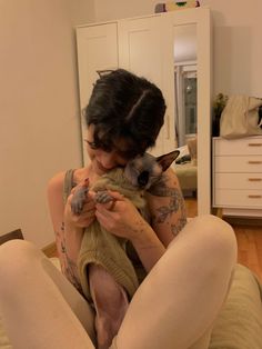 a woman holding a cat in her arms while sitting on the floor next to a mirror