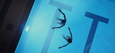 two people are swimming in the pool with their feet on the glass floor and one person is diving into the water