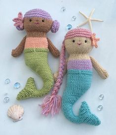 two knitted mermaid dolls sitting next to each other on top of a white sheet