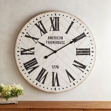 an american farmhouse clock on the wall above a dresser and vase with flowers in it